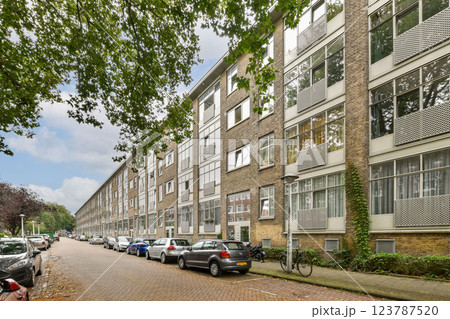 A view of a modern residential street lined with trees and buildings. Cars are parked along the road, showcasing urban living. 123787520