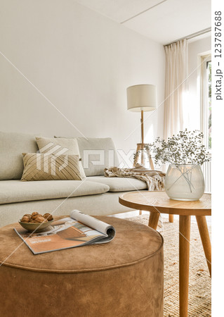 A stylish and cozy modern living room featuring neutral tones, a circular coffee table, and elegant decor elements like flowers and cushions. 123787688