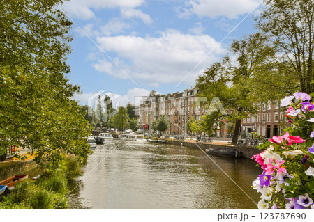 A picturesque canal view framed by vibrant flowers and lush green trees, showcasing boats and charming buildings along the waterway. 123787690