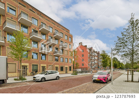 Features a modern residential street with well-designed buildings, greenery, and parked cars, showcasing urban architecture and lifestyle. 123787693