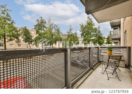 A contemporary balcony view featuring green trees lining the street, along with a simple table and chair setup, creating a serene outdoor space. 123787956