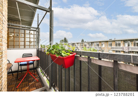 A bright, inviting balcony featuring a small red table and chair, adorned with potted plants, creating a serene outdoor space for relaxation. 123788201