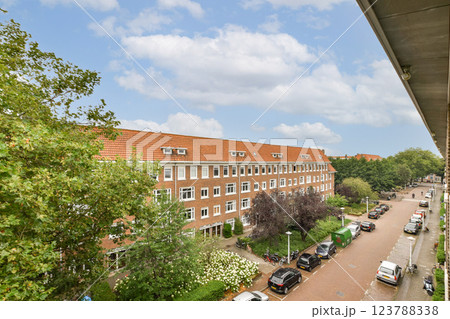 A picturesque view of a residential block adorned with lush greenery, accompanied by parked cars along a tree-lined street under a bright sky. 123788338