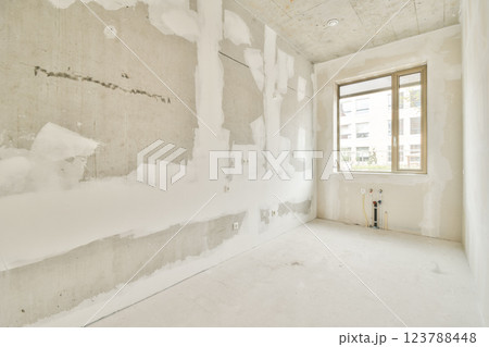 Empty room with unfinished walls, natural light streaming through a window, showcasing a minimalist design and construction phase. Empty room with unfinished walls, natural light streaming through a window, showcasing a minimalist design and construction phase. 123788448