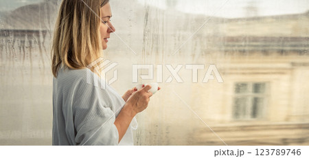 Woman in elegant robe drinking coffee in hotel room and standing near window 123789746