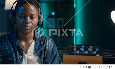 Teleworker enjoying music while researching data for company project, doing tasks in personal home office overnight. Woman sitting at desk in front of laptop and using headphones, camera A 123789747