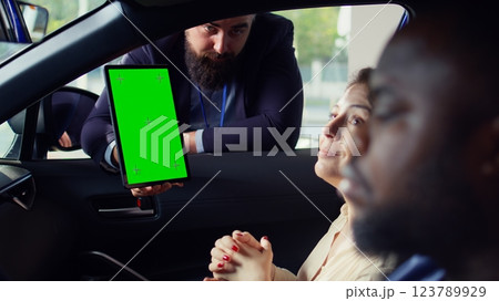 Showroom salesman showing stat charts on green screen tablet to clients after test drive. Dealership agent showing vehicle driving metrics graphs on chroma key device to couple, camera B 123789929