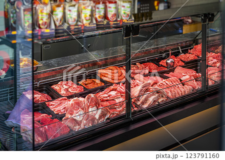 Meat counter. Butcher shop fridge counter with assortment of raw meat.. Glass display case in butcher shop filled with fresh meat products. Various cuts of beef, pork, sausages are arranged for buyers 123791160