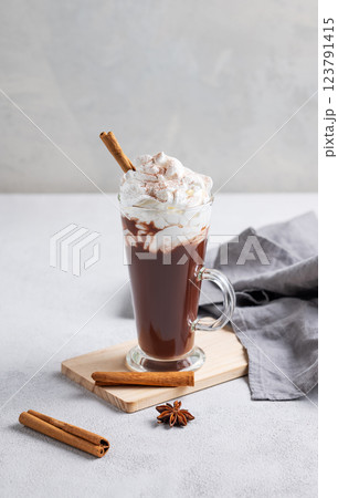 Hot chocolate with whipped cream, cinnamon and spices in a tall glass on a light background. 123791415