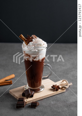 Hot chocolate with whipped cream, cinnamon and spices in a tall glass on a dark background. Hot chocolate with whipped cream, cinnamon and spices in a tall glass on a dark background. 123791417