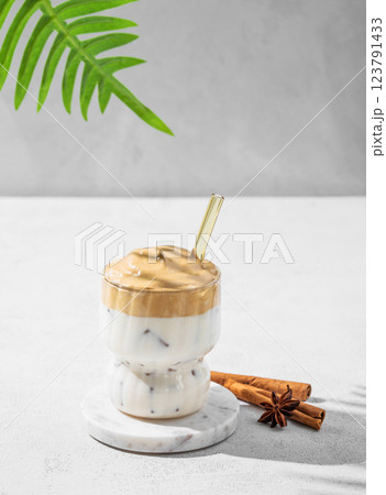 Dalgona coffee  in a glass on a light background with palm leaf, shadow and spices. 123791433