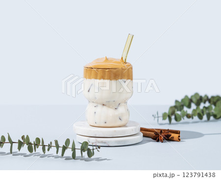 Korean whipped drink Dalgona coffee on a marble stand on a blue background with cinnamon. Korean whipped drink Dalgona coffee on a marble stand on a blue background with cinnamon. 123791438