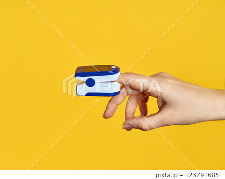 Pulse Oximeter digital device on finger measuring oxygen saturation over yellow background. 123791685