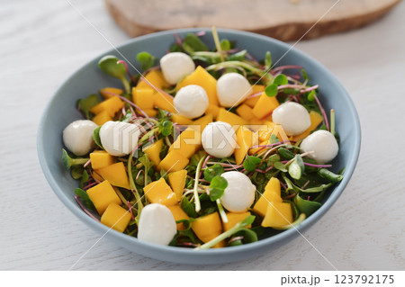 Salad with mango, mozzarella and mixed microgreens in blue bowl on white oak table 123792175