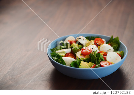 Salad with avocado, cherry tomatoes, romaine and mozzarella in blue bowl on walnut table with copy space Salad with avocado, cherry tomatoes, romaine and mozzarella in blue bowl on walnut table with copy space 123792188