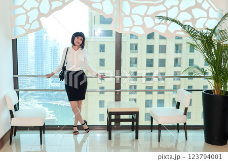 A woman in a business suit is waiting for an elevator in a multi-story building, standing at a panoramic window 123794001