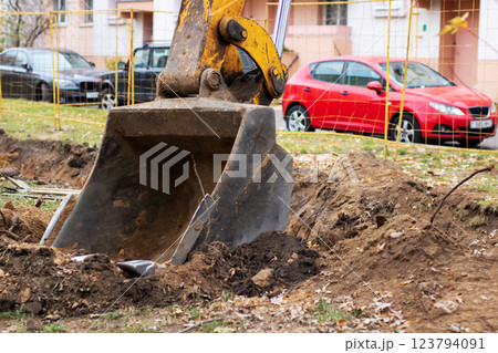 A bright yellow excavator is actively digging a hole in the ground A bright yellow excavator is actively digging a hole in the ground 123794091
