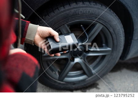 Close up of man hand holds a wireless portable air pump for inflating car tires. Self service, maintenance and safety.  123795252