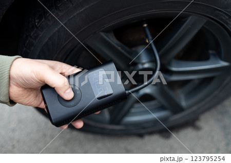 Close up of man hand holds a wireless portable air pump for inflating car tires. Self service, maintenance and safety.  123795254