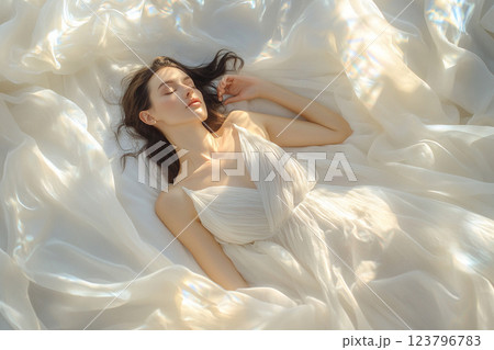 serene woman in flowing white dress lies gracefully on soft, shimmering fabric, embodying tranquility and elegance. gentle light enhances ethereal atmosphere serene woman in flowing white dress lies gracefully on soft, shimmering fabric, embodying tranquility and elegance. gentle light enhances ethereal atmosphere 123796783