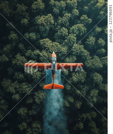 Aerial view of orange airplane flying over dense green forest, leaving trail of smoke. contrast between vibrant aircraft and lush trees creates striking visual Aerial view of orange airplane flying over dense green forest, leaving trail of smoke. contrast between vibrant aircraft and lush trees creates striking visual 123796891