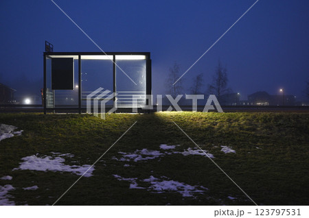 A minimalist bus stop illuminated by glowing panels on a foggy evening 123797531