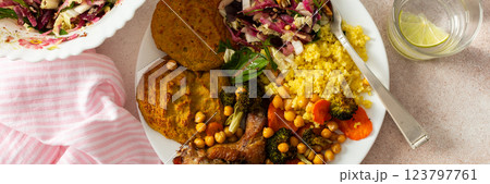 A nutritious, hearty breakfast of lentil zucchini pancakes, millet, baked chicken neck, roasted sweet potatoes, broccoli, carrots, chickpeas, with a fresh salad of radish, sprouts, and nuts, banner 123797761