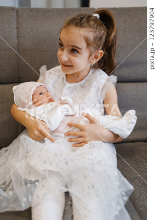 Newborn baby in a hat with pink lace in the arms of his sister in a white dress 123797904