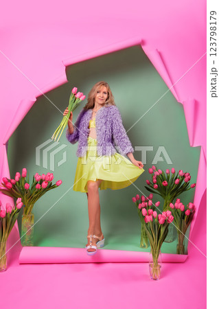 A beautiful elderly woman with a bouquet of tulips comes out of a torn pink background. 123798179