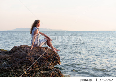 Woman relaxing on rock contemplating inspiring ocean view at sunset Woman relaxing on rock contemplating inspiring ocean view at sunset 123798202