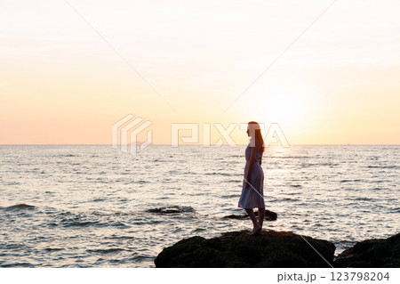 Silhouette of a young woman on rocks by the sea, enchanted by the sunset and ocean view 123798204
