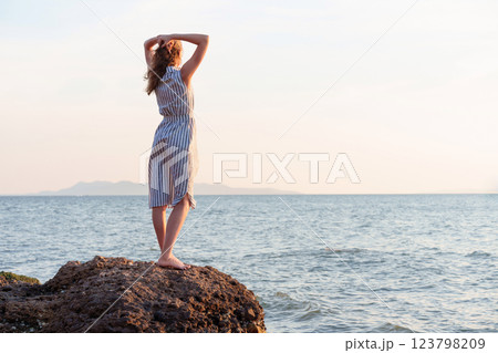 Young woman holding hair enjoying sunset on rock by the sea 123798209