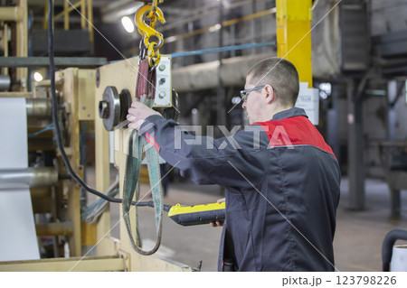 A worker at a factory turns on the installation of an overhead crane to lift a load. 123798226