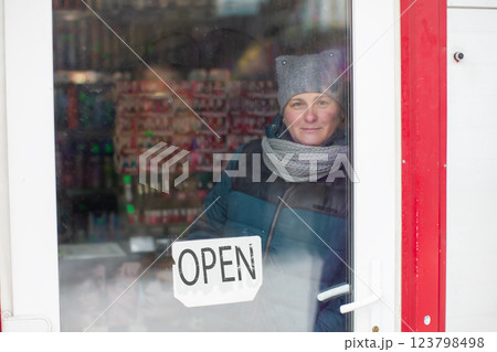 A woman looks through the glass door of a store marked "open." 123798498