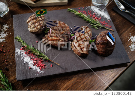 Succulent grilled steaks with flags of Brazil, Uruguay, and Estonia. Presented with herbs and microgreens on a slate plate, perfect for a fine dining experience in a gourmet restaurant 123800142
