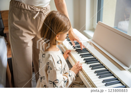 Home lesson with teacher on music for girl on white piano synthesizer. Concept of early development: learning music enhances motor skills, hearing, intelligence, fostering creativity from childhood 123800883