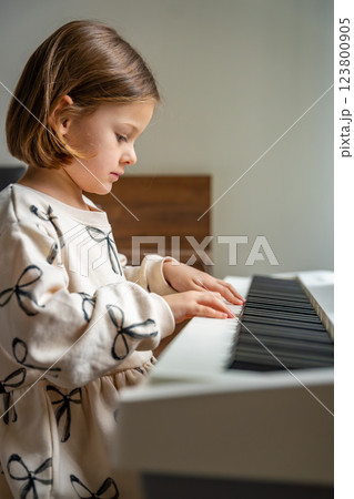 Home lesson on music for the girl on white piano synthesizer. Concept of early development: learning music enhances motor skills, hearing, and intelligence, fostering creativity from childhood Home lesson on music for the girl on white piano synthesizer. Concept of early development: learning music enhances motor skills, hearing, and intelligence, fostering creativity from childhood 123800905