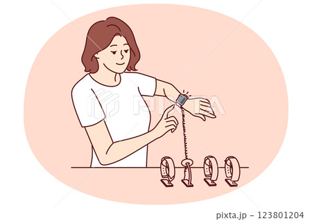 Woman tries on smart watch or fitness bracelet, wanting to choose device for playing sports Woman tries on smart watch or fitness bracelet, wanting to choose device for playing sports 123801204