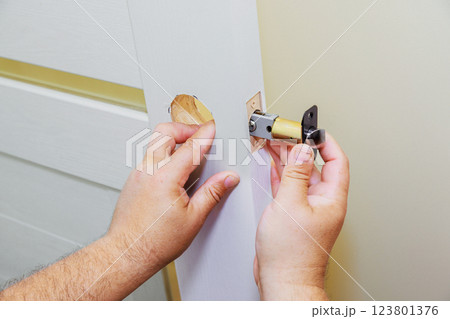 Hands installing lock cylinder into door at home during renovation Hands installing lock cylinder into door at home during renovation 123801376