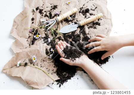 Childrens hands gardening with soil and tools on brown paper with flowers 123801455
