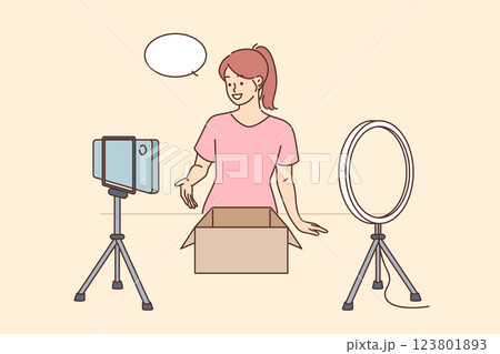 Woman blogger makes unpacking packages from advertiser, stands near table with phone  123801893