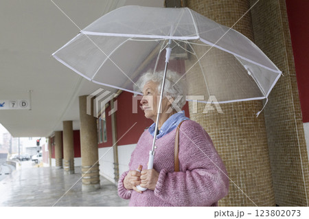 Elderly woman holding transparent umbrella walking in rainy city Elderly woman holding transparent umbrella walking in rainy city 123802073