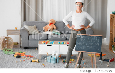 Cleaning, living room and blackboard with a woman mother in her home to clean up children toys off of the floor. Mom, cleaner and mess with a strict female in messy lounge with a helmet and goggles 123802959