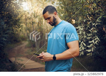 Sports man, phone and runner in a forest taking a break while texting, communication and typing a message while out for a run. Male athlete out for workout in woods using technology to track health 123802978