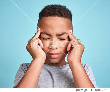 Child with headache, stress and mental health problem or fatigue pain on blue studio background. Frustrated african american kid, depressed boy and angry youth with fingers massaging temples of head Child with headache, stress and mental health problem or fatigue pain on blue studio background. Frustrated african american kid, depressed boy and angry youth with fingers massaging temples of head 123803237