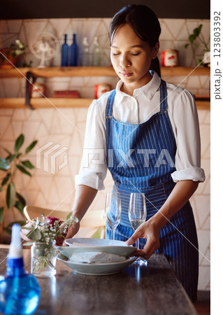 Waitress, restaurant and clean at table for plate, glass and cutlery in apron at work. Woman, cafe or coffee shop cleaning with hands after lunch, dinner or meal with customer dishes in Cape Town 123803392
