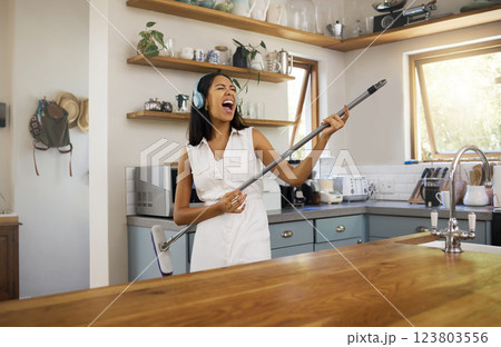 Cleaning, headphones and black woman singing and playing air guitar music with a broom in a house. Fun, playful and happy female enjoying a clean home, kitchen or room while streaming song or radio 123803556