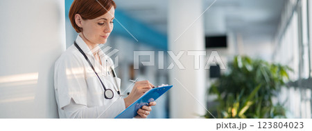 Portrait of woman doctor in hospital hallway, holding medical records in hand. Portrait of woman doctor in hospital hallway, holding medical records in hand. 123804023