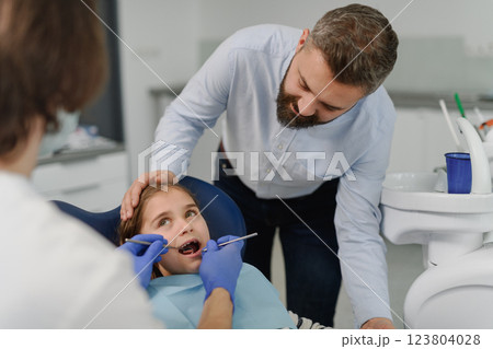 Girl during annual dental check-up in dental clinic, father supporting her. 123804028