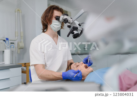 Male dentist doing dental procedure in dental clinic, using dental microscope. Male dentist doing dental procedure in dental clinic, using dental microscope. 123804031